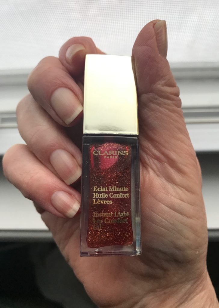 Clarins Instant Light Lip Comfort Oil square gold topped bottle with clear glass showing the red oil with gold flecks, neversaydiebeauty.com