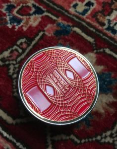 view of the top of Mirabella Pure Press Mini Compact to show the red and gold design details, neversaydiebeauty.com
