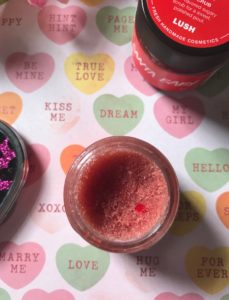 open LUSH Santa Baby Lip Scrub showing a tiny red edible heart in the scrub, neversaydiebeauty.com