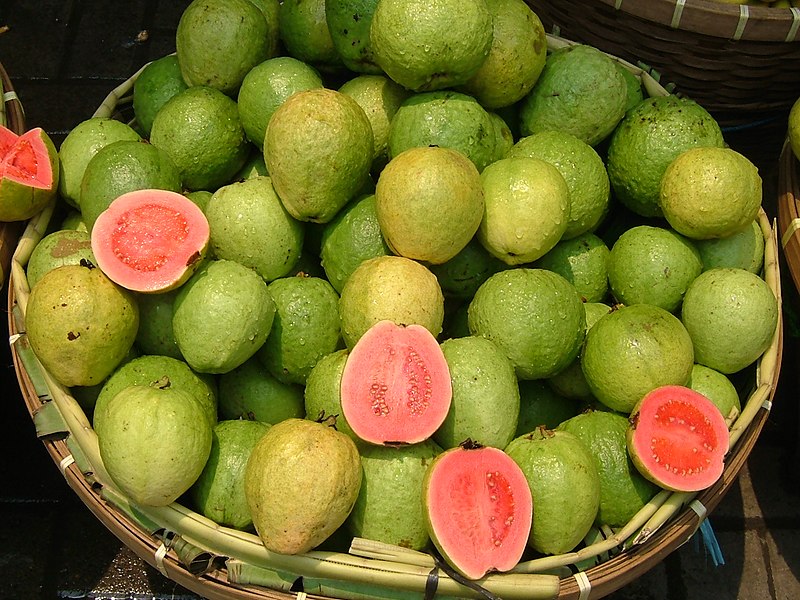 photo of guava fruit in a basket with several guavas cut open to reveal the bright pink flesh inside