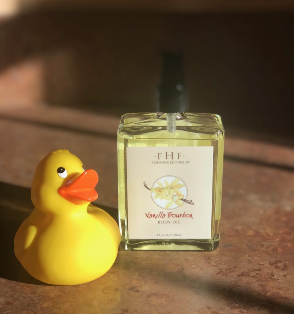 clear glass pump bottle of gold Farmhouse Fresh Vanilla Bourbon Body Oil with a yellow rubber duck nearby, neversaydiebeauty.com