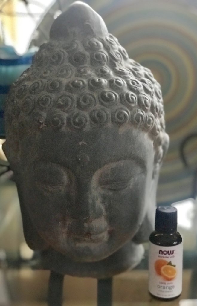 Buddha head with NOW Foods orange essential oil bottle, neversaydiebeauty.com