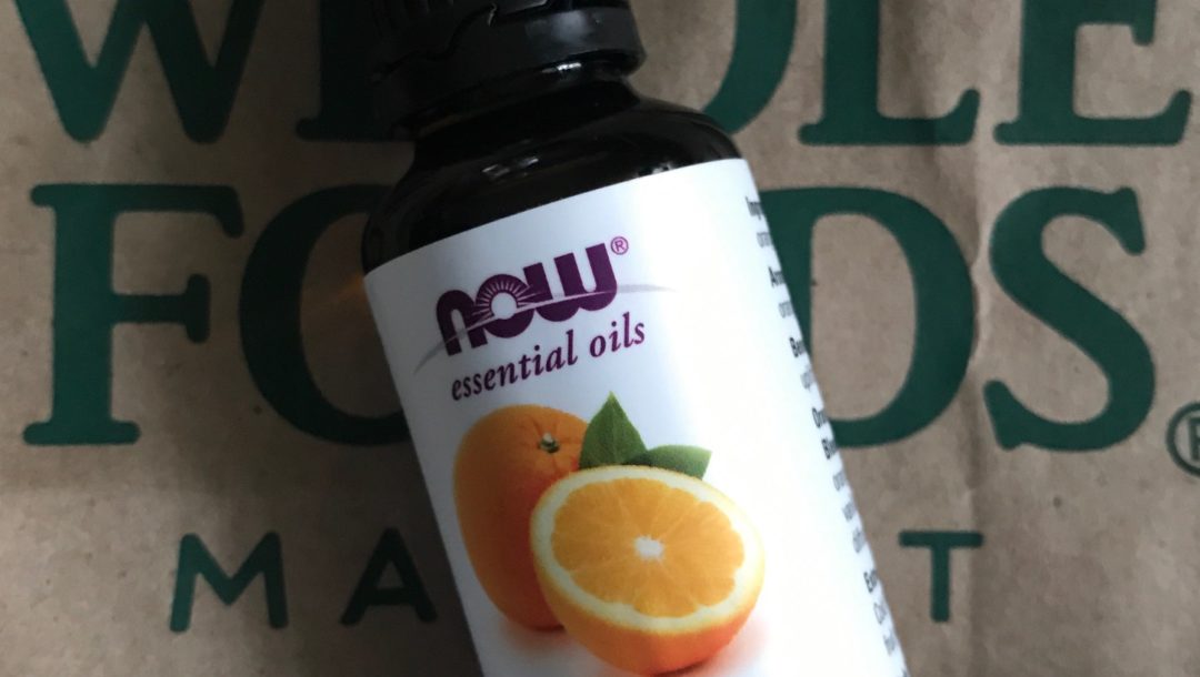 NOW Foods orange essential oil against a Whole Foods bag, neversaydiebeauty.com