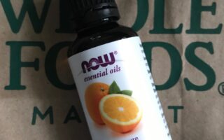 NOW Foods orange essential oil against a Whole Foods bag, neversaydiebeauty.com