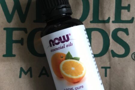 NOW Foods orange essential oil against a Whole Foods bag, neversaydiebeauty.com