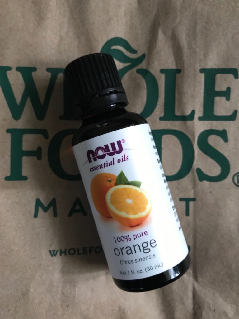 NOW Foods orange essential oil against a Whole Foods bag, neversaydiebeauty.com