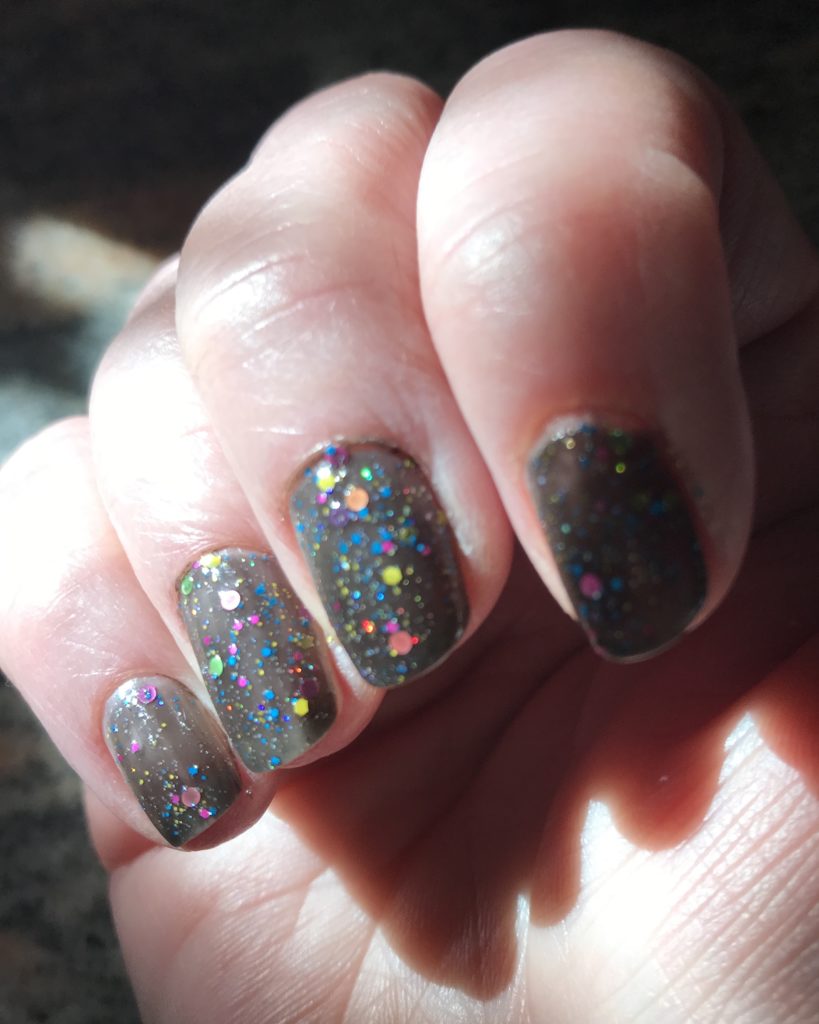bright sunlight shining on my nails wearing Glam Polish "We Will Rock You 2.0", a black crelly polish with iridescent glitter and pastel round flakes, neversaydiebeauty.com
