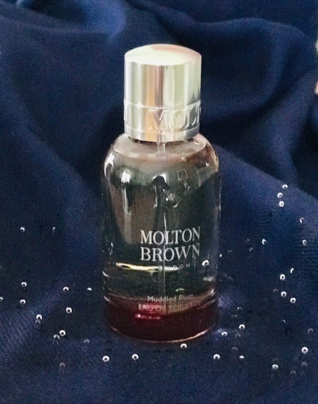 bottle of Molton Brown LE Muddled Plum eau de toilette against a dark blue background, neversaydiebeauty.com
