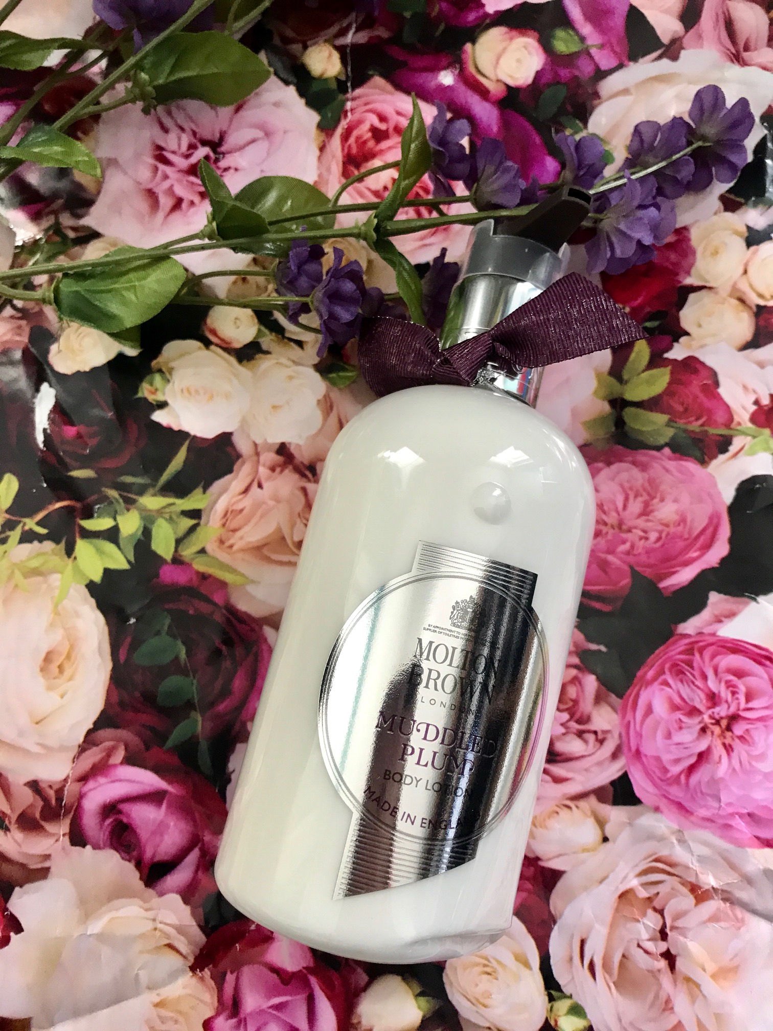 bottle of Molton Brown Muddled Plum Body Lotion against a flowered background, neversaydiebeauty.com