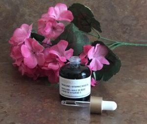 green glass dropper bottle of Biossance Squalane Vitamin C Rose Oil, open to show the clear oil in the dropper