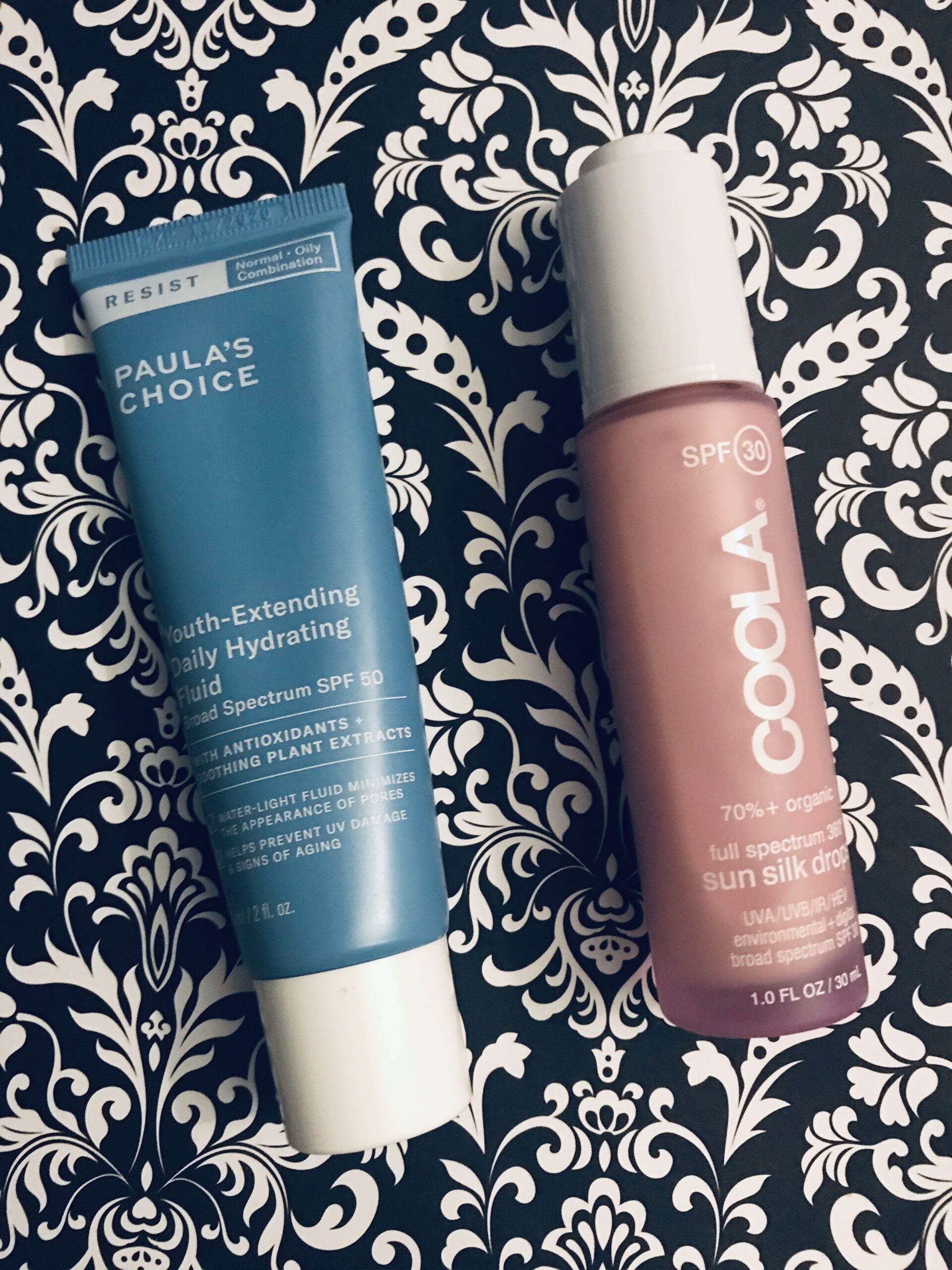 tube of Paula's Choice Youth Extending Hydrating Fluid SPF 50 and bottle of Coola Sun Silk Drops SPF 30