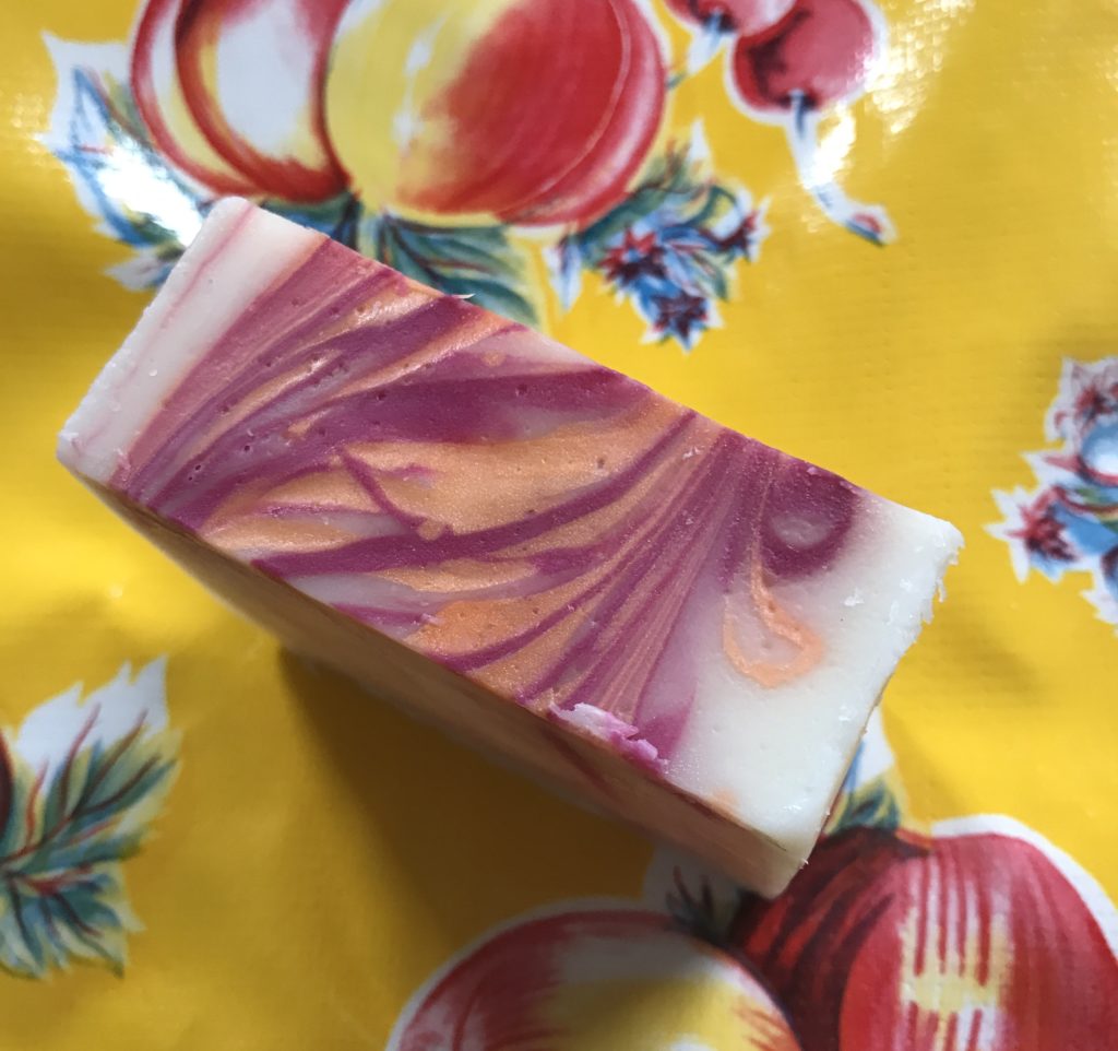 the top of a bar of Nature Island Botanicals Pomegranate Mango Bar Soap showing the red and peach colors within the white background