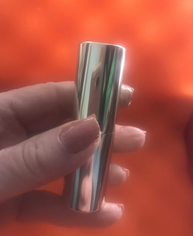 my hand holding a silvery gold tube of BECCA Ultimate Lipstick Love