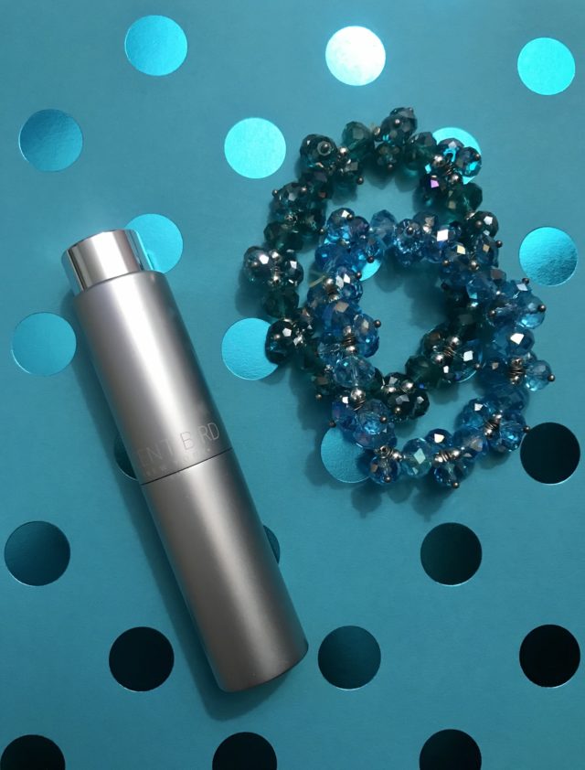 silvertone Scentbird metal tube case against teal background with bracelets
